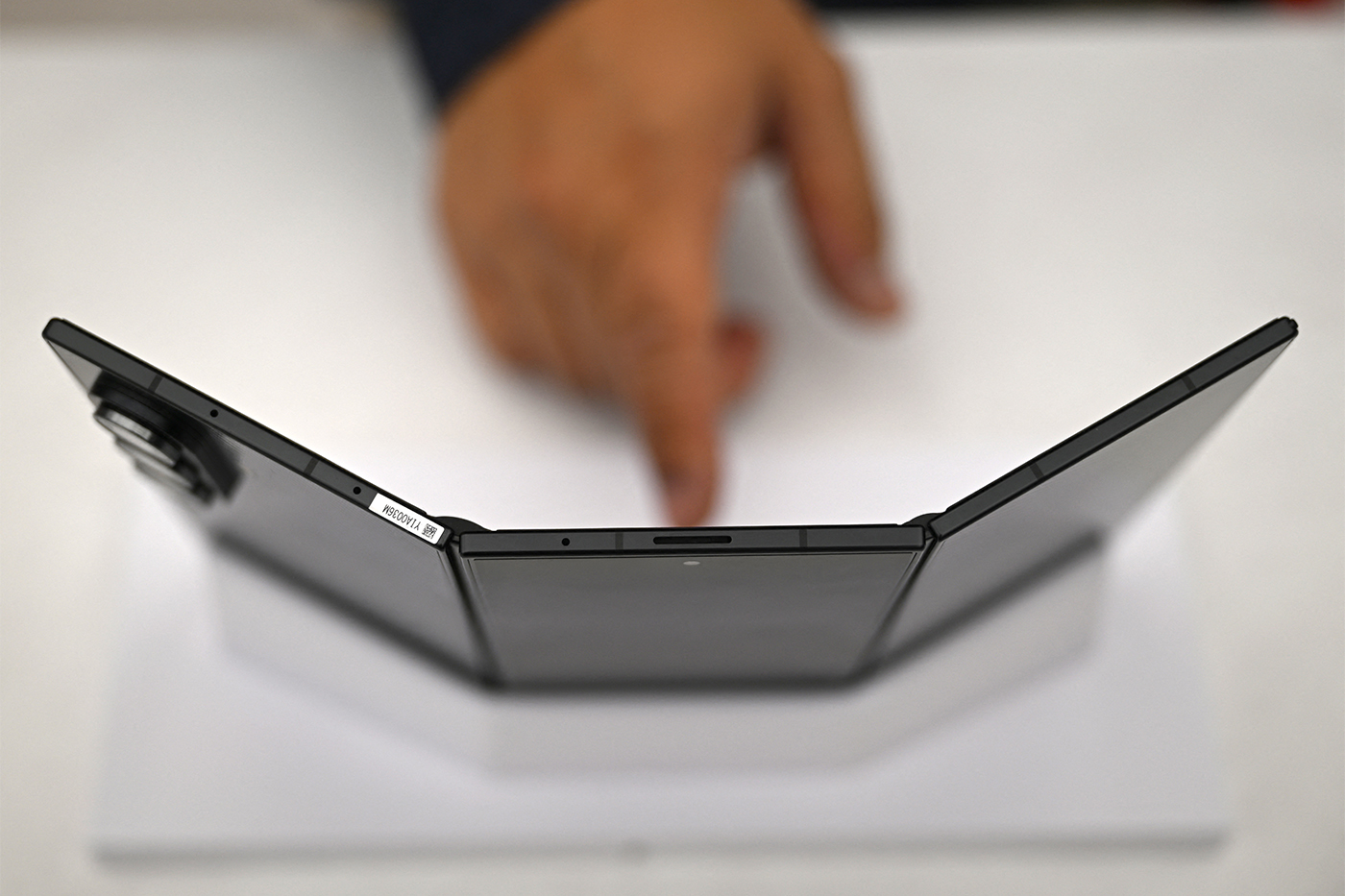 A person points their finger at at a phone with three screens propped up.