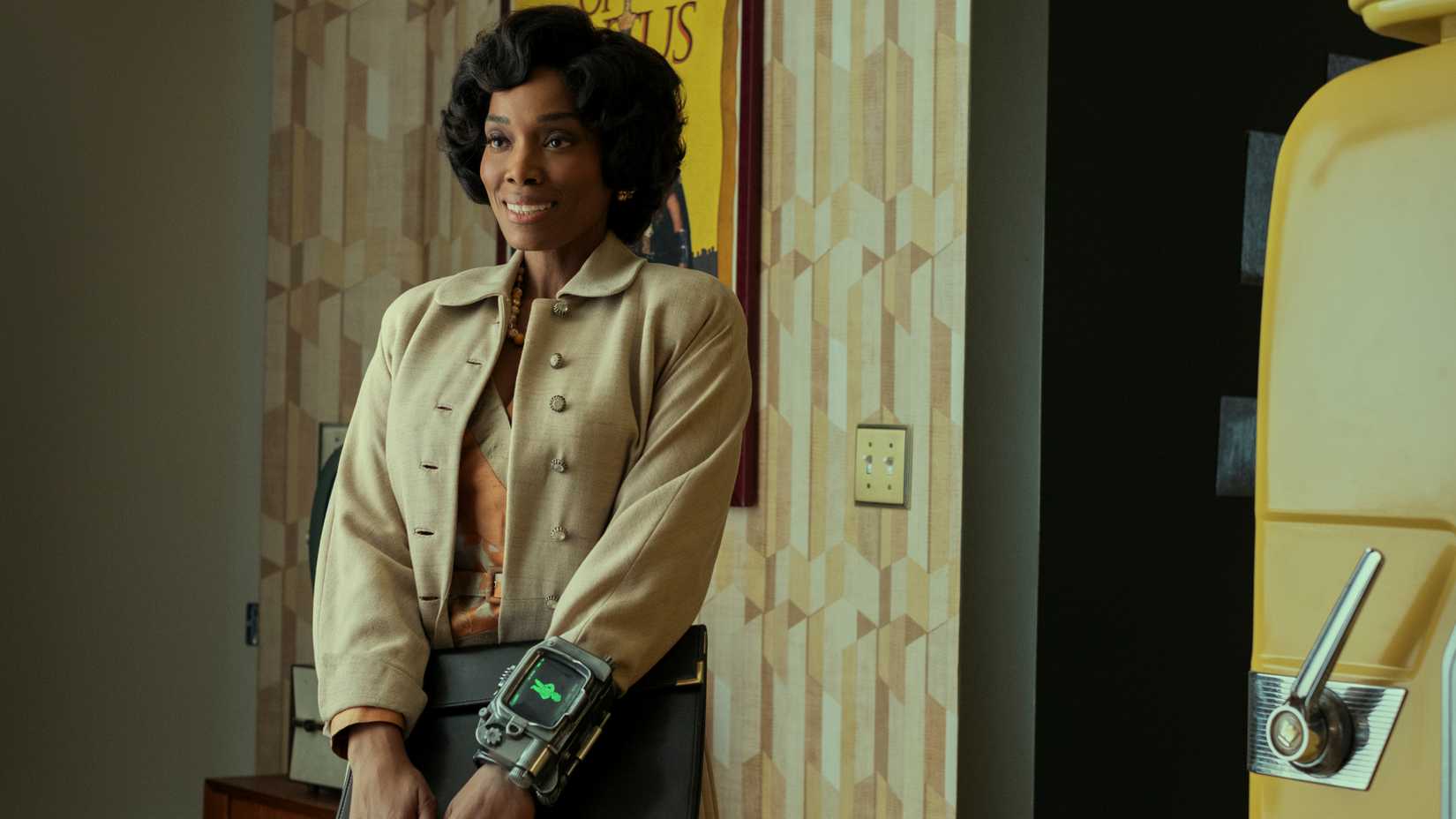 Frances Turner as Barb Howard standing and smiling with a Pip-Boy on her wrist in Fallout