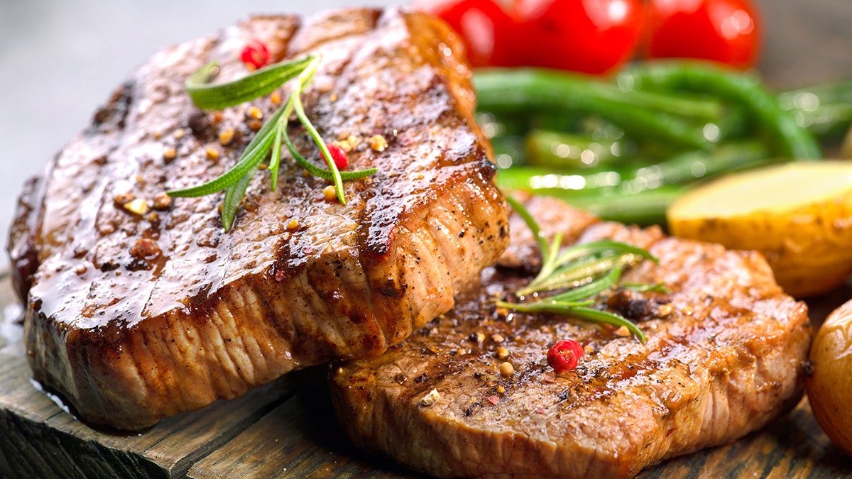 Grilled beef steaks seen garnished with veggies and potatoes in background
