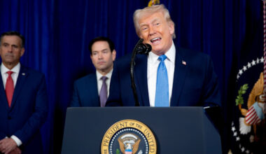 US President Donald Trump speaks at a podium during a news conference, with two unidentified men standing behind him.