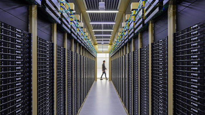 Rows of black server racks line a corridor in the Naver Data Center at GAK Chuncheon, with a person walking in the distance