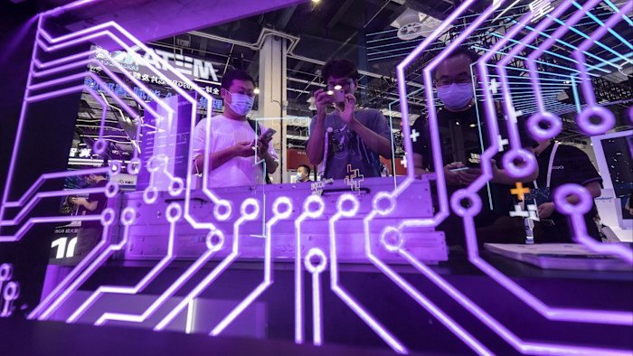 Several attendees, some wearing masks, interact with devices at the MetaX LLC booth behind a glowing purple circuit board display.