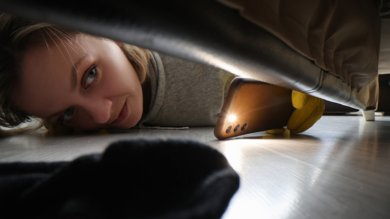 A person using the light on an Android phone to look under the couch.