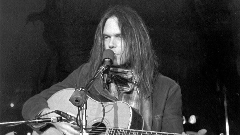Neil Young onstage with microphone and acoustic guitar