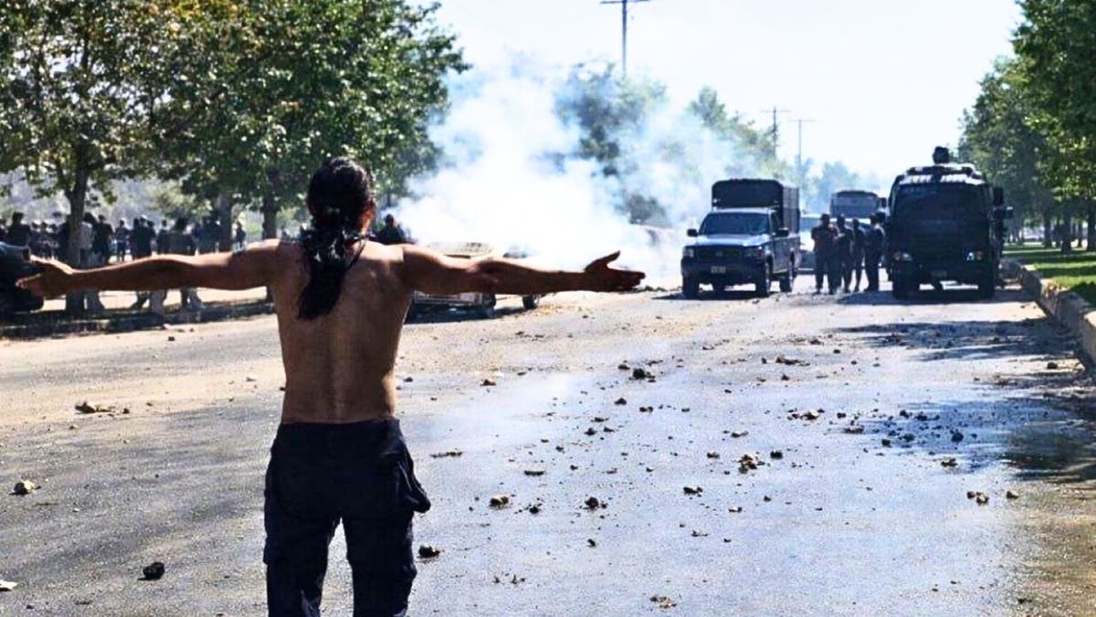 A protester stands facing Iranian security vehicles during clashes.