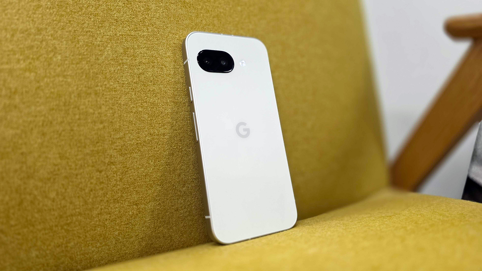 Google's Pixel 9a in the Porcelain color option leaning against a mustard armchair