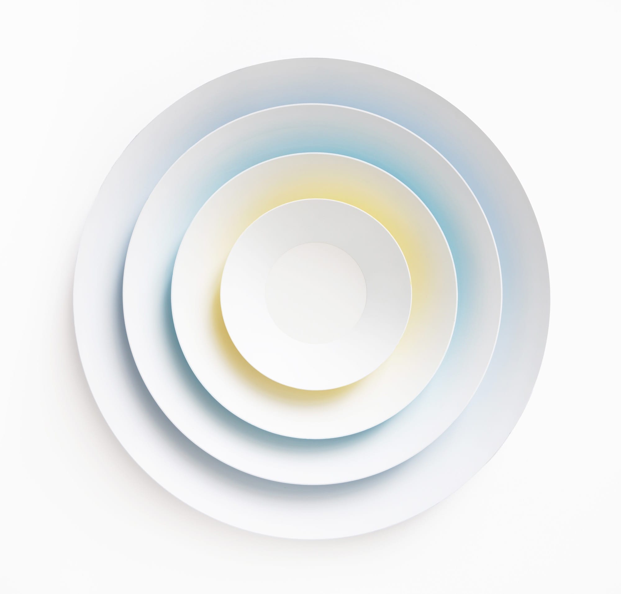 a sculpture by Luftwerk with white concentric rings that glow in blue and yellow from the underside