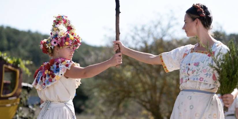 Florence Pugh as Dani, wearing a flower crown and holding a stick with another woman in 'Midsommar'