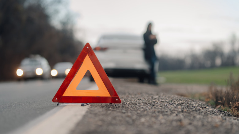 a driver waiting at the side of a road near an orange warning triangle