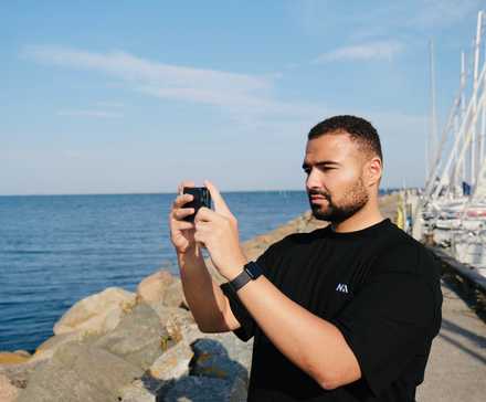 A man taking photos on their smartphone while standing next to the ocean