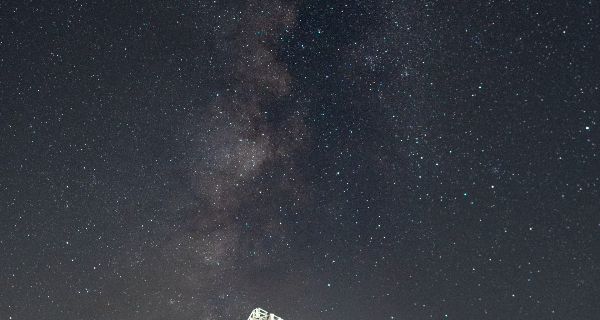 A white radio antenna faces upward in the direction of a star-studded night sky.