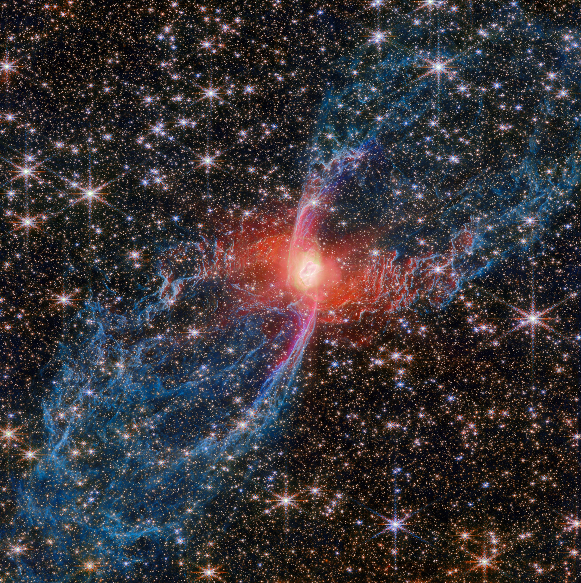 A bright, red-hued nebula with symmetrical blue filaments is surrounded by numerous stars in deep space, as JWST reveals the universe’s hidden wonders.