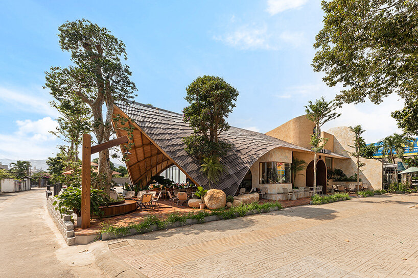 rippling metal roof drapes over interlocking stone volumes of vietnamese café
