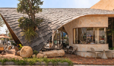 rippling metal roof drapes over interlocking stone volumes of vietnamese café