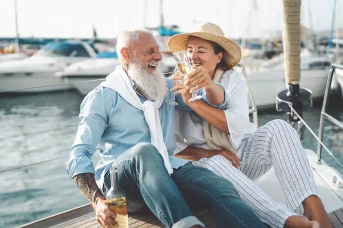 Senior couple toasting champagne on sailboat vacation - Happy elderly people having fun celebrating wedding anniversary on boat trip - Love relationship and travel lifestyle concept.