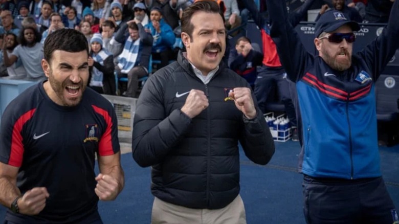 Roy Kent (Brett Goldstein), Ted (Jason Sudeikis) and Coach Beard (Brendan Hunt) cheering in Ted Lasso