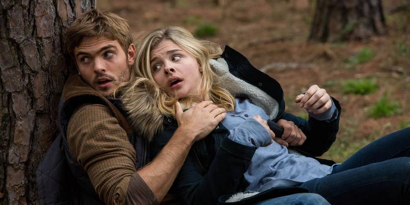 Chloe Grace Moretz as Cassie Sullivan and Alex Roe as Evan Walker taking cover behind a tree in a forest in 'The 5th Wave'