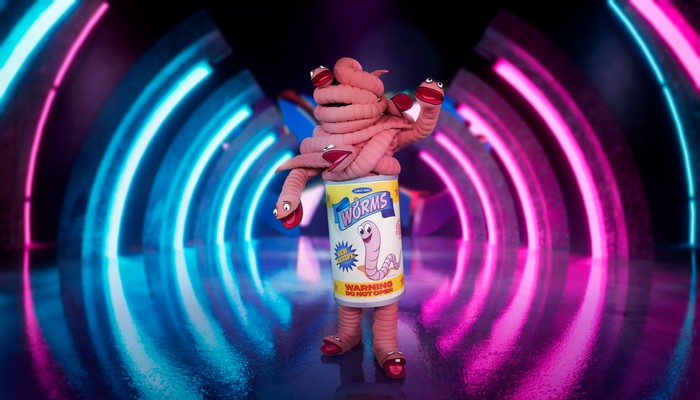Someone dressed up as a can of worms, stood on a stage with blue and pink lighting.
