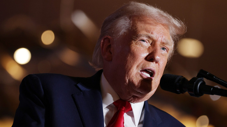 President Donald Trump, his left eye slightly closed and mouth open as he talks into a microphone.