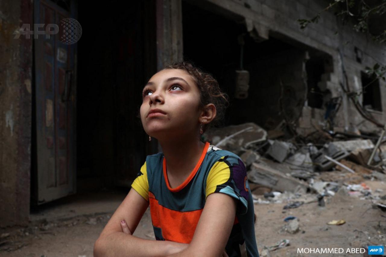 A young Palestinian girl sits in front of her home in Gaza City which was damaged by Israeli bombardment on May 20, 2021. (AFP Photo )