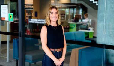 A young white woman with blonde hair wearing a black top is smiling.
