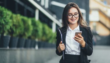 An investor walks down a city street and looks at something on a smartphone.