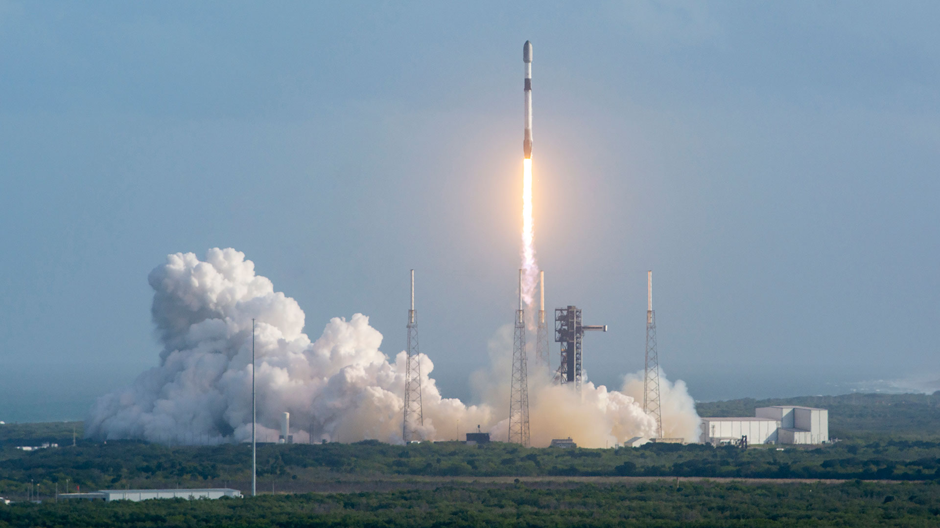 a white and black rocket lifts off from its launch pad, leaving a large white plume