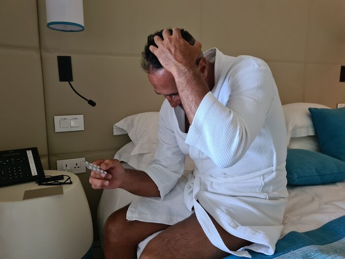 Man in hospital robe sitting on bed looking stressed, holding medication, depicting patients leaving hospital against medical advice.