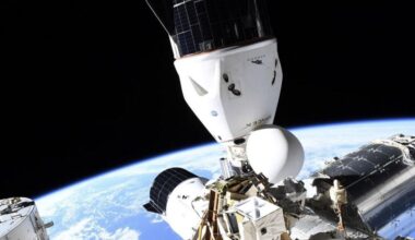 two white spacecraft are seen docked at different orientations on a space station, floating above Earth.