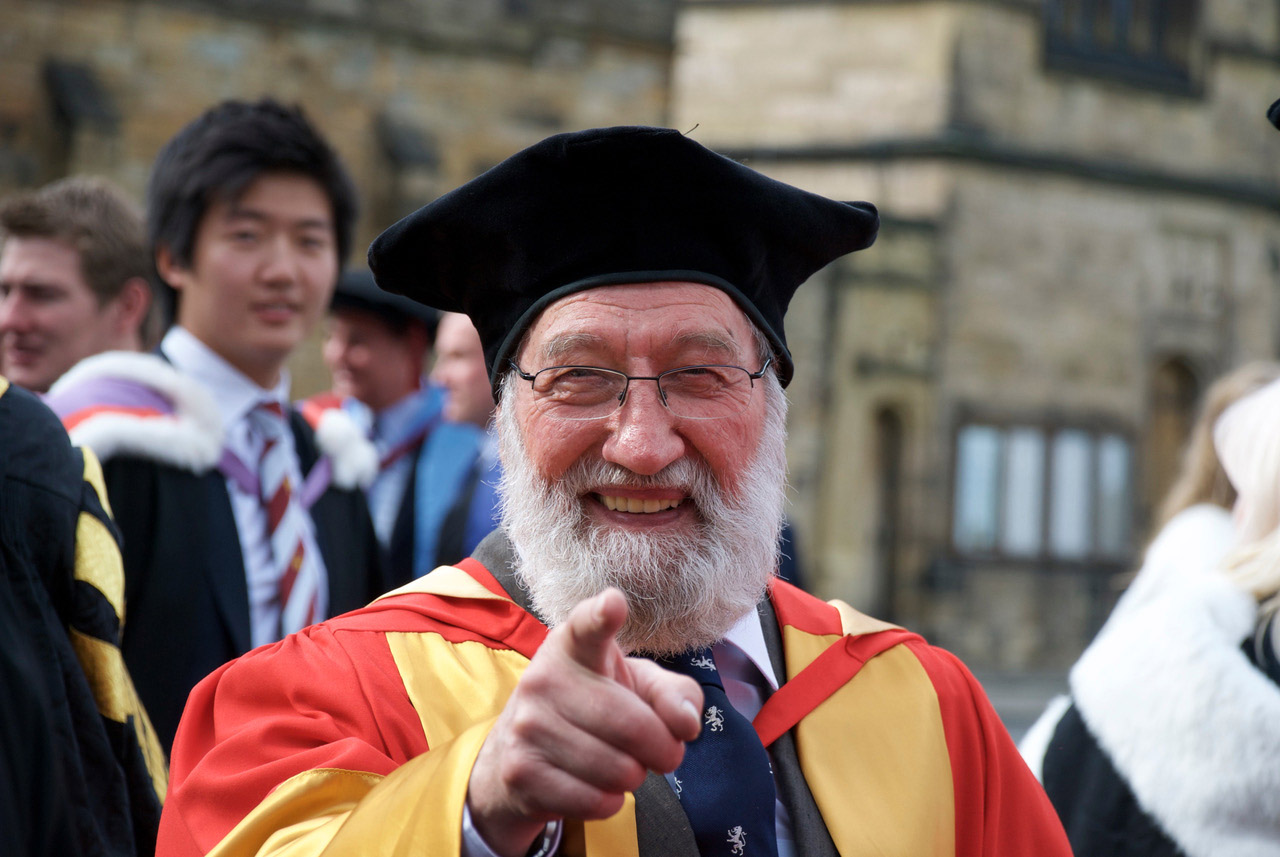 Dr. Fenwick Lawson in academic regalia, smiling and pointing at the camera.
