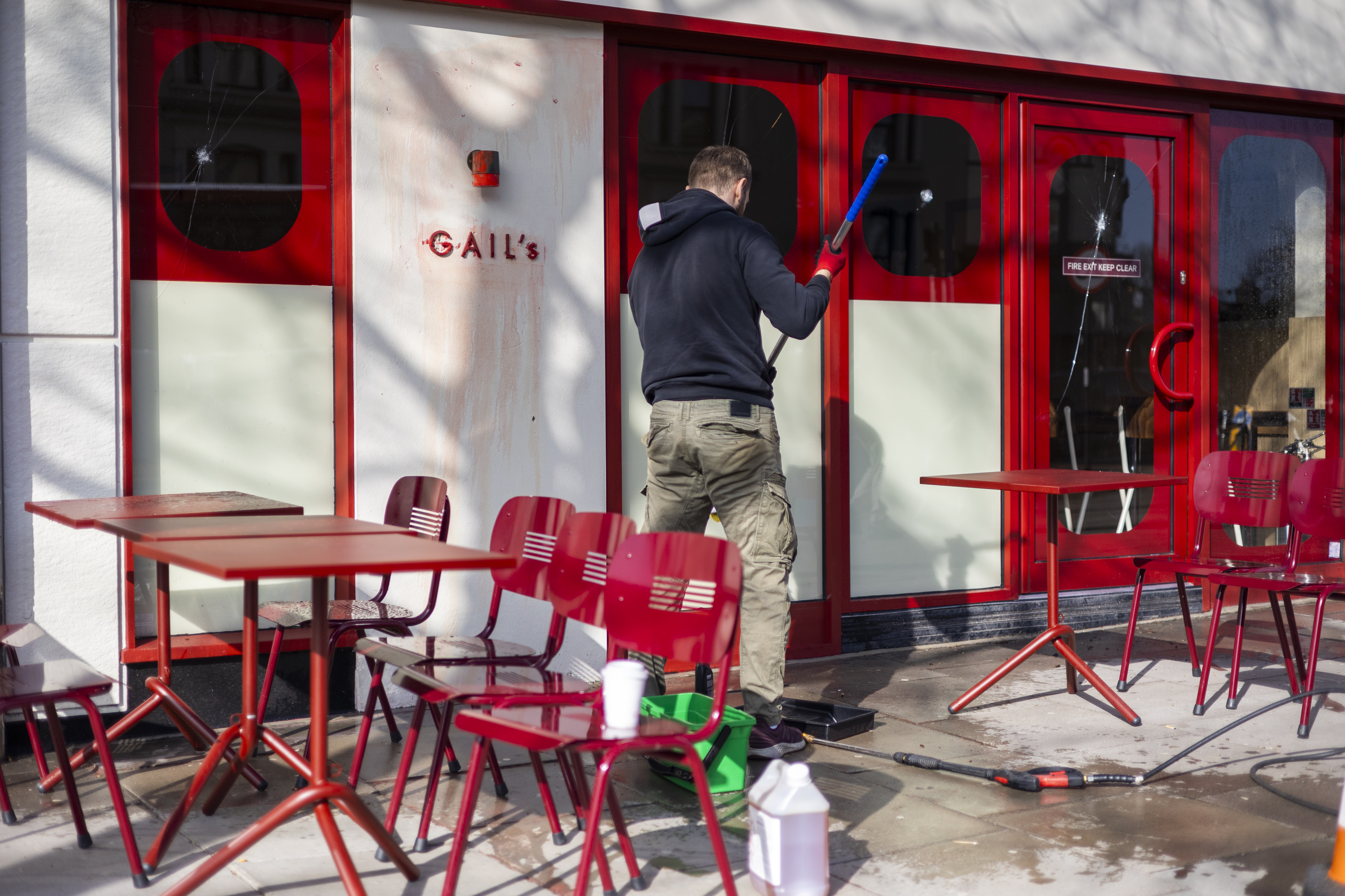 A man cleans anti-Semitic graffiti from the wall of a Gail's bakery and cafe, whose window is also smashed.