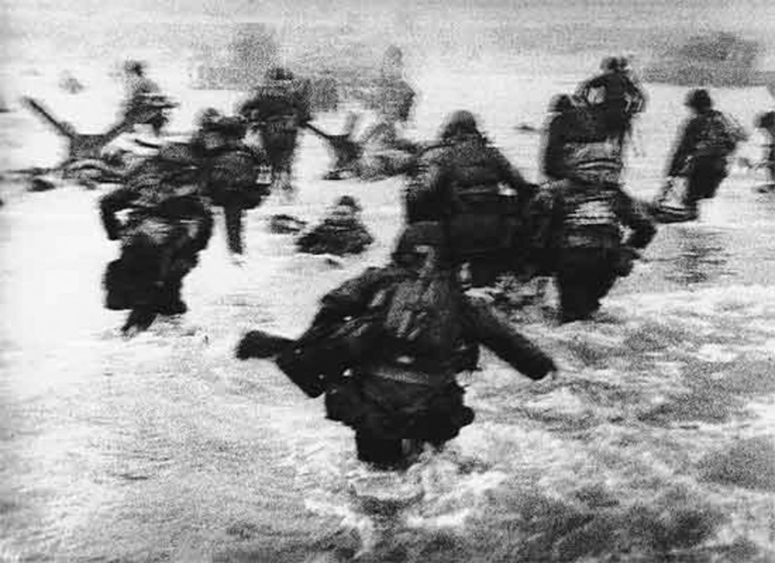 Soldiers advancing through shallow water on a beach.