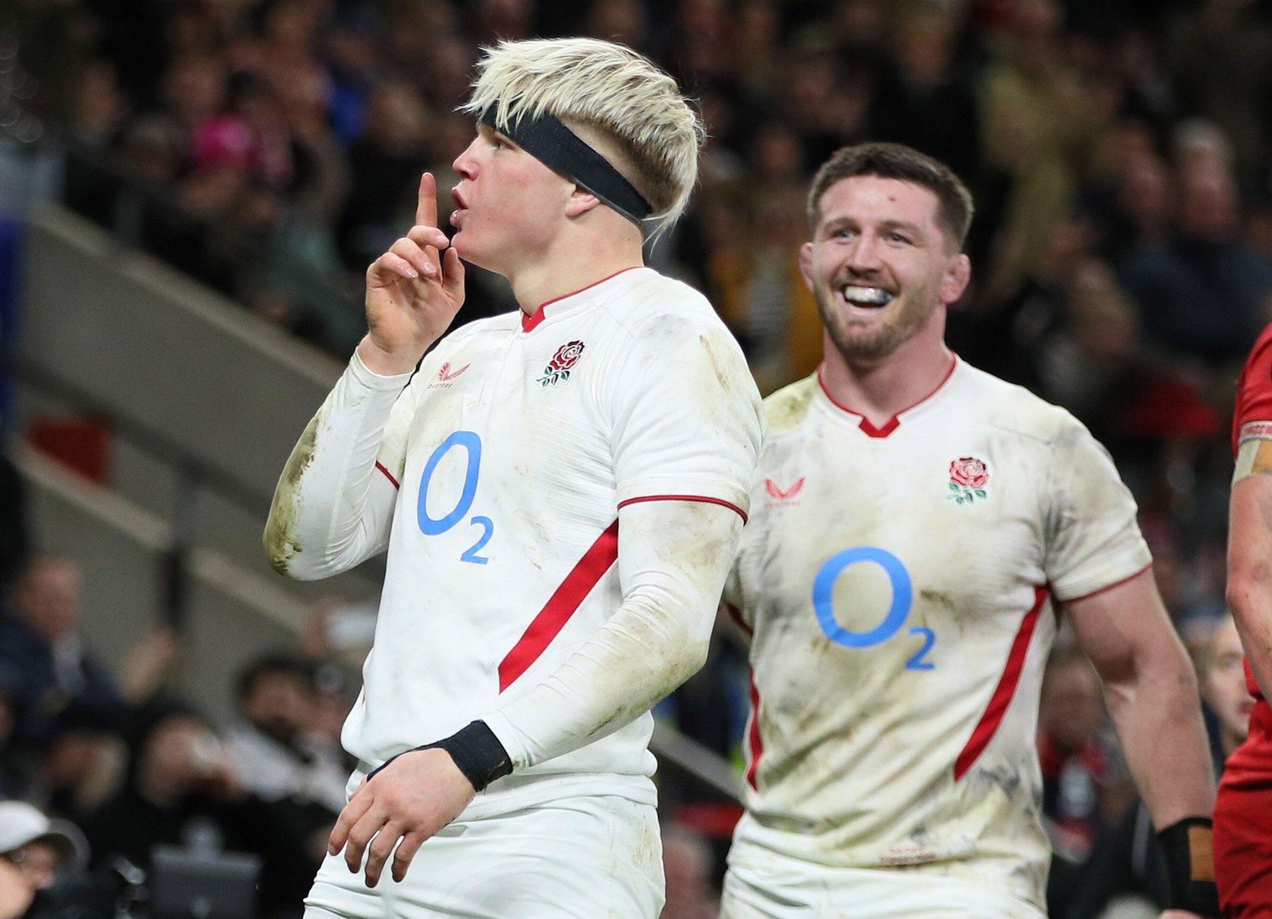 Henry Pollock of England celebrating scoring a try with a "shhh" gesture, with another player smiling behind him.