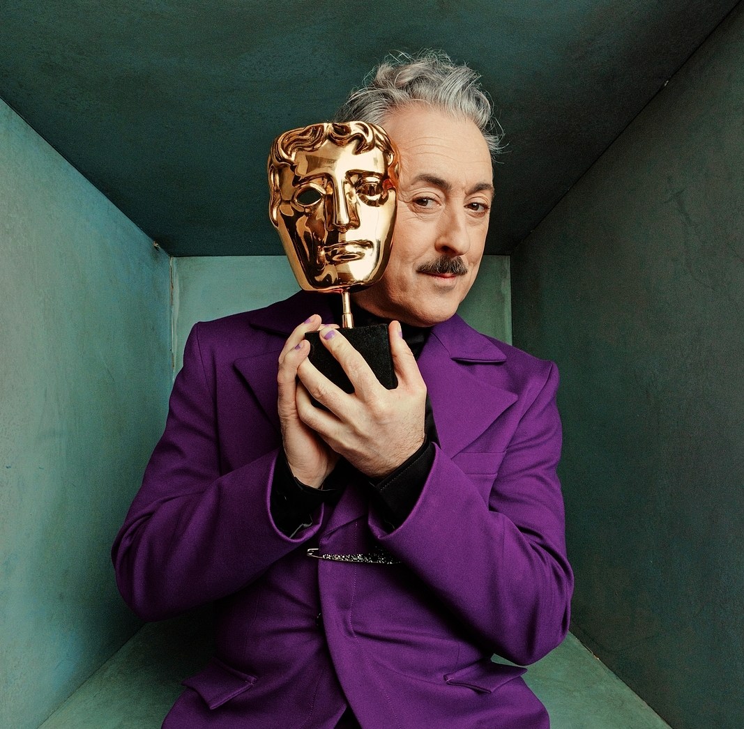 Alan Cumming holding a BAFTA award.