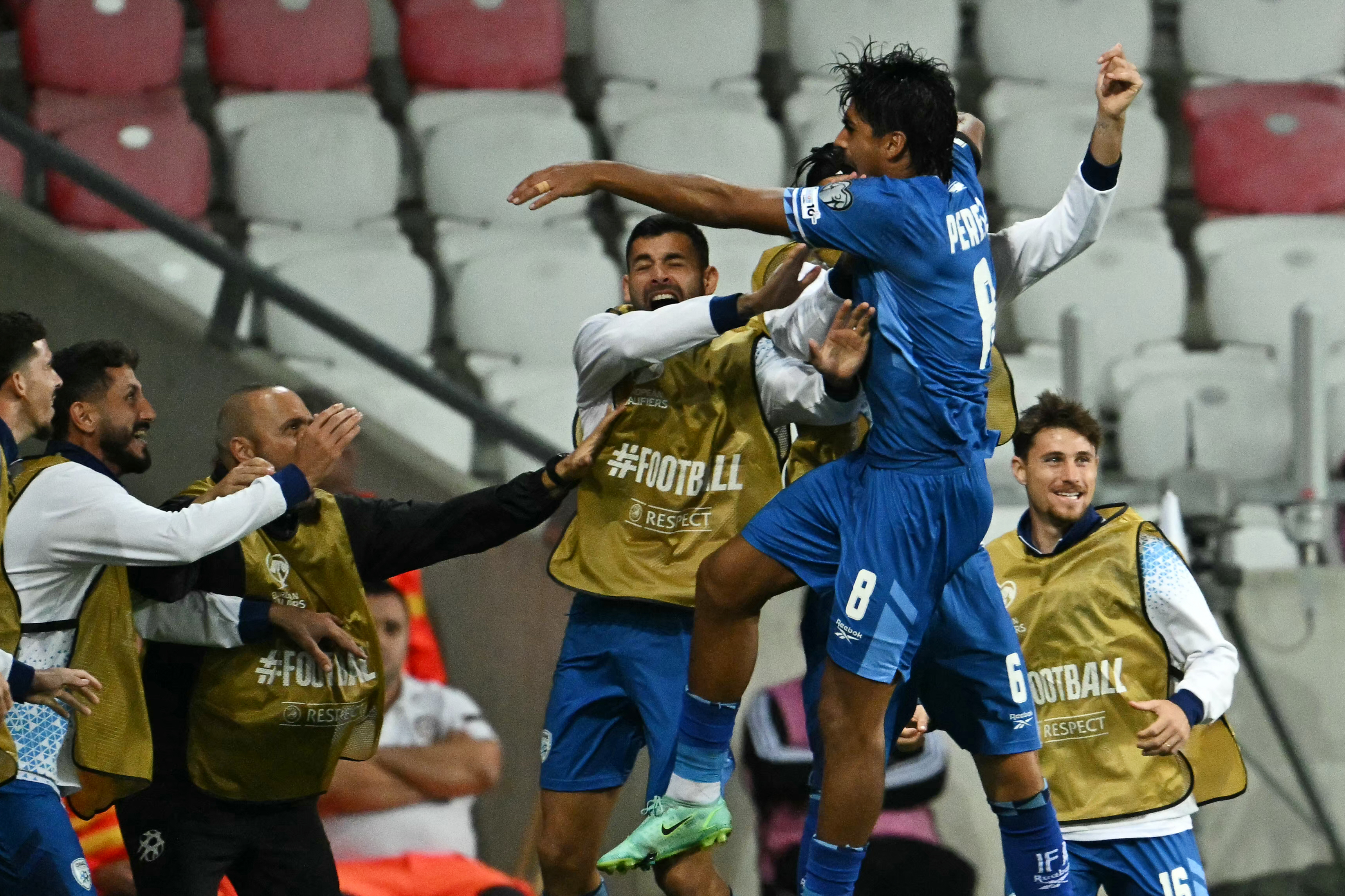 Israeli midfielder Dor Peretz celebrating a goal with teammates, all in blue and white uniforms.
