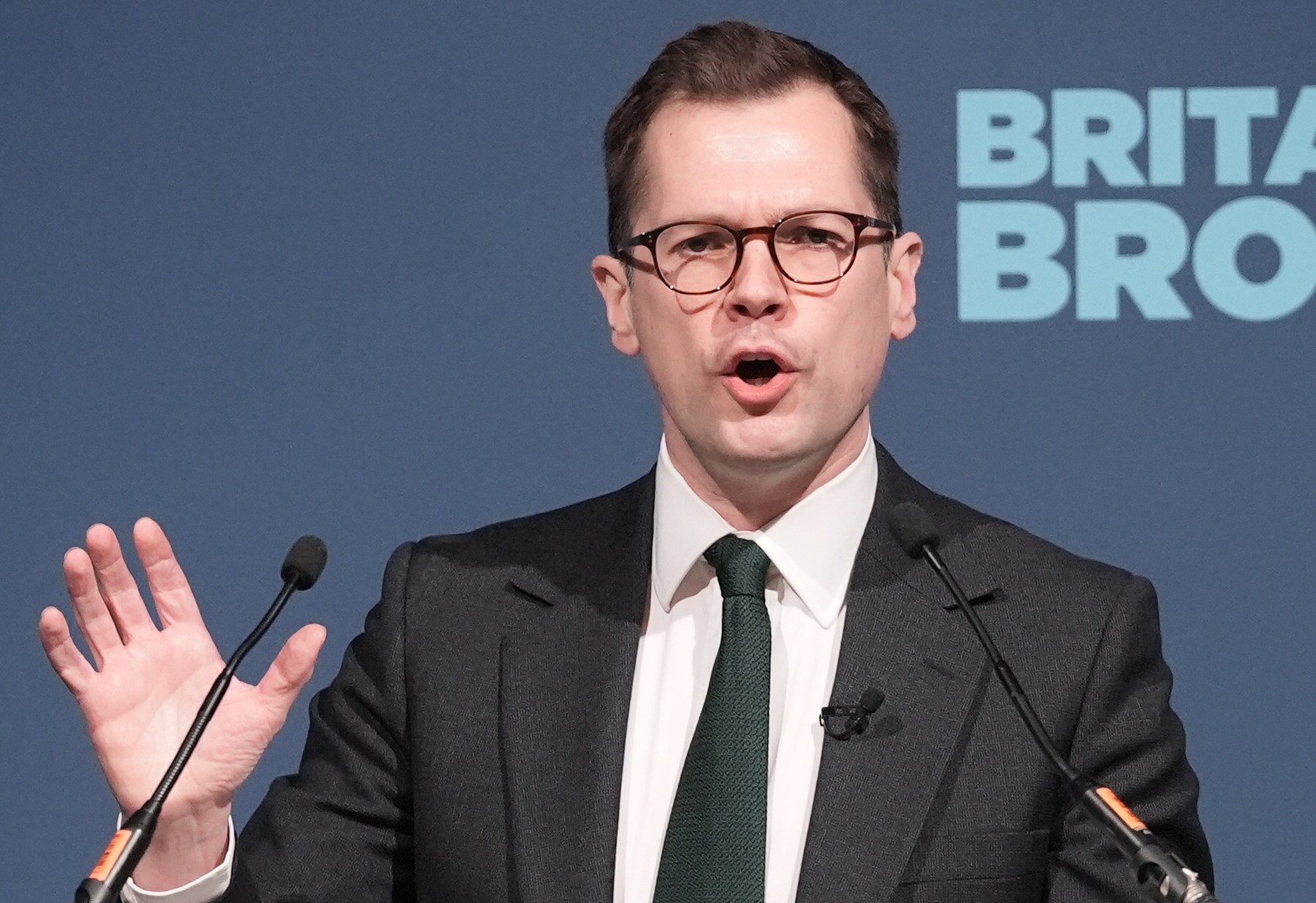 Robert Jenrick speaking at a podium with "BRITAIN NEEDS REFORM" written on it.