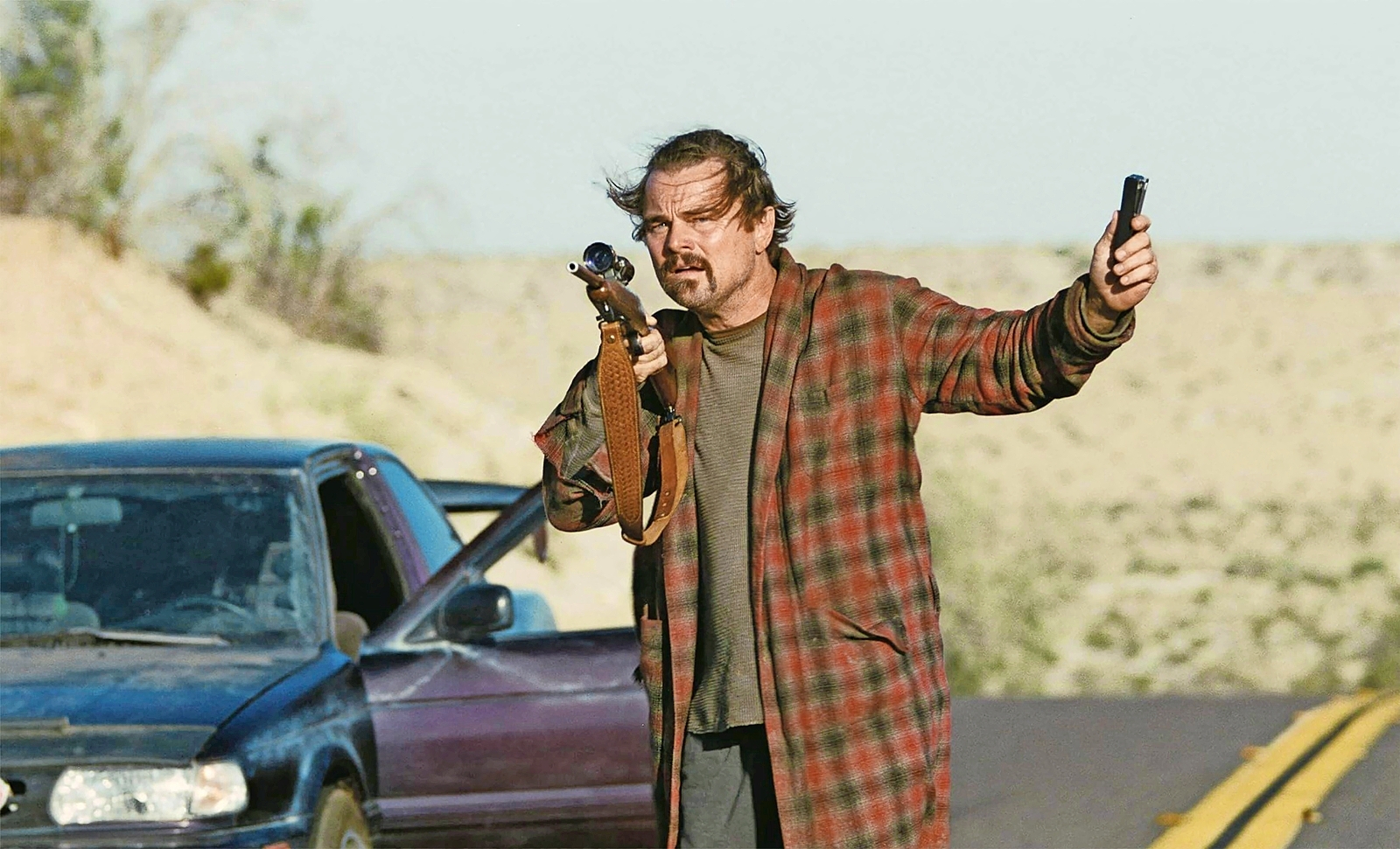 Leonardo DiCaprio as Bob Ferguson holding a rifle and a phone in "One Battle After Another."