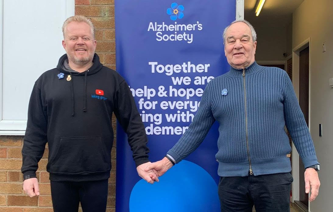 Paul Lindsay and his father Richard holding hands in front of an Alzheimer's Society banner.