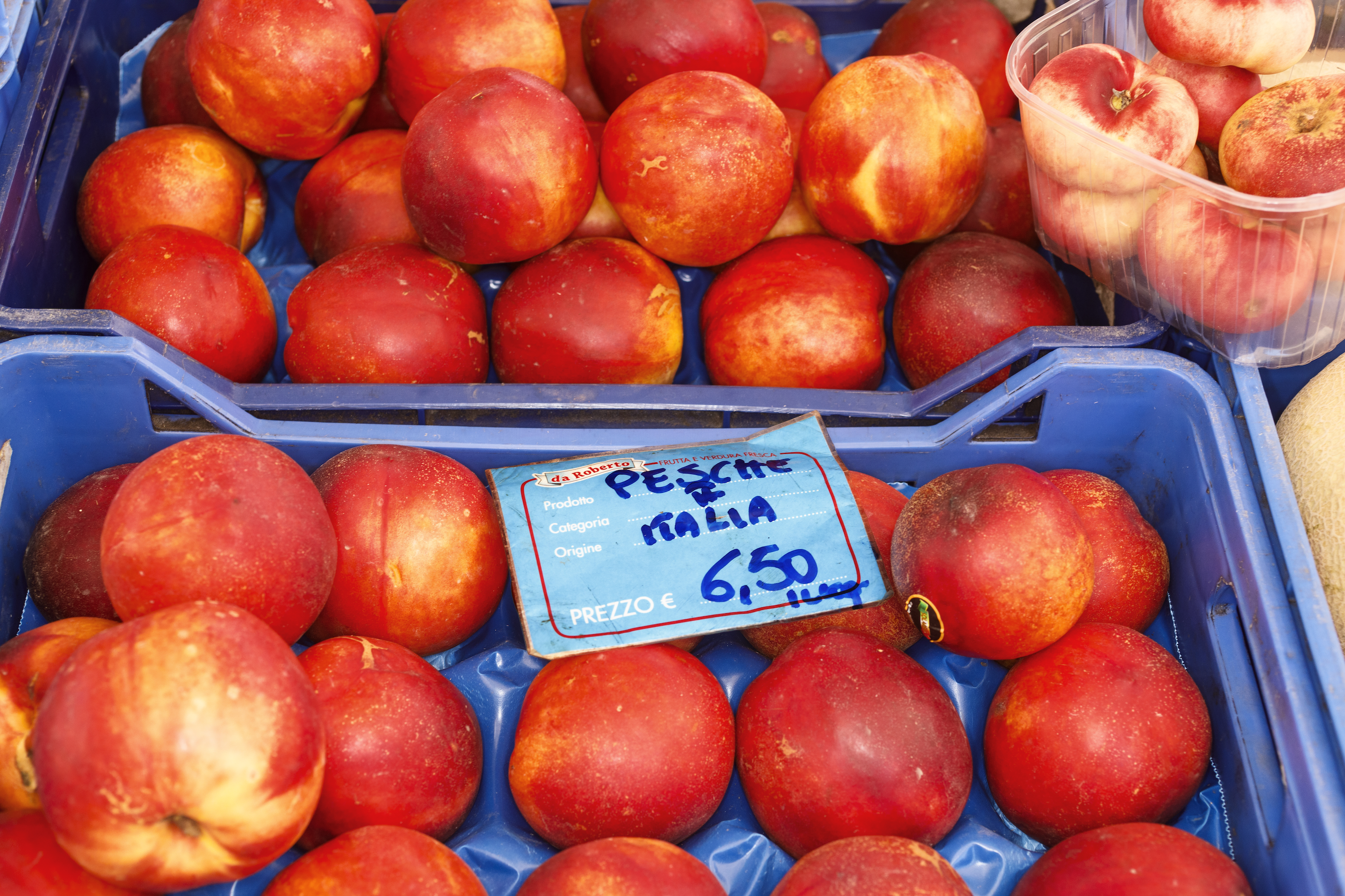 Peaches for sale, originating from Italy and priced at 6.50 euros, displayed in blue crates.