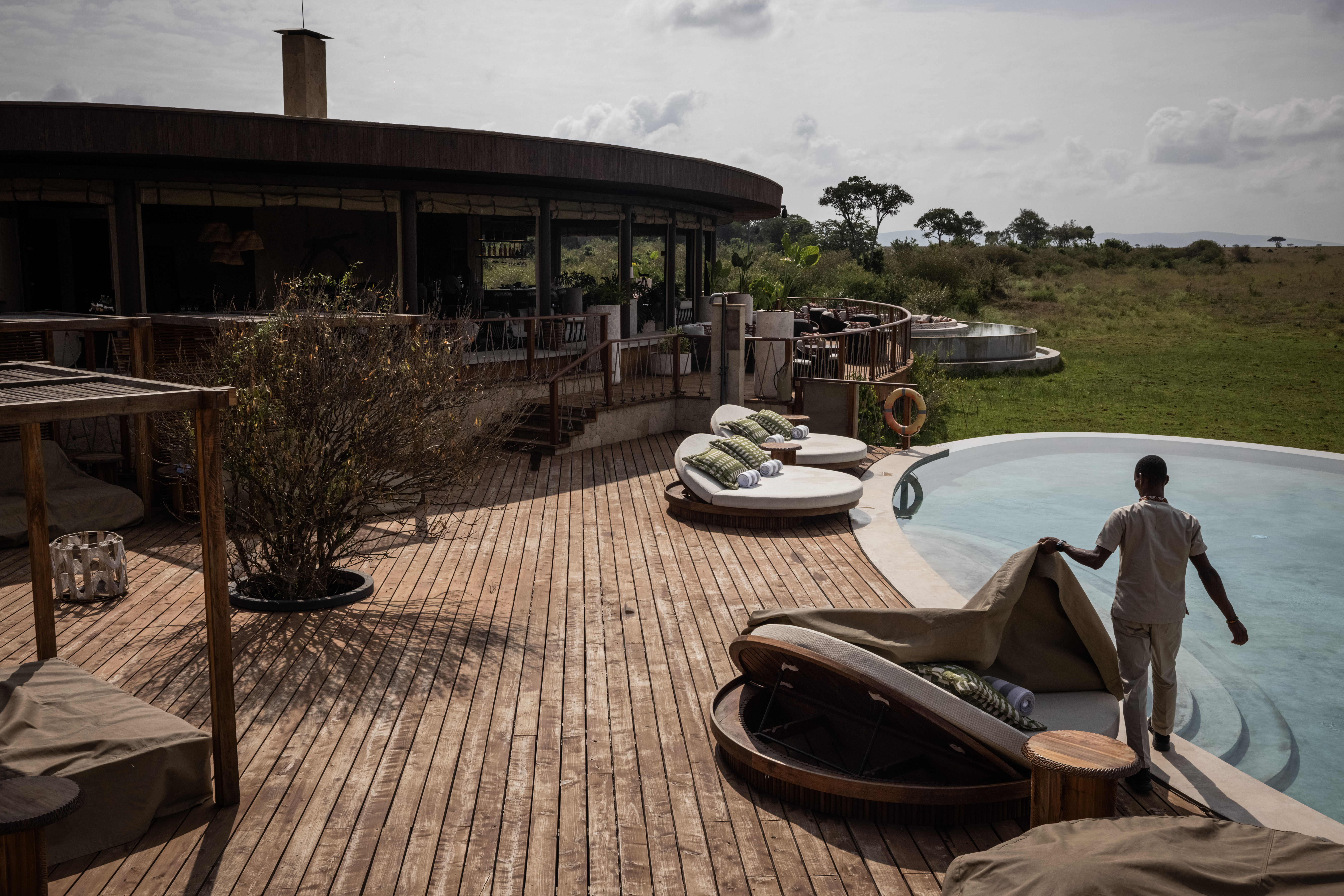 A hotel worker removes a cover from a sun bed next to a pool, overlooking the Serengeti.