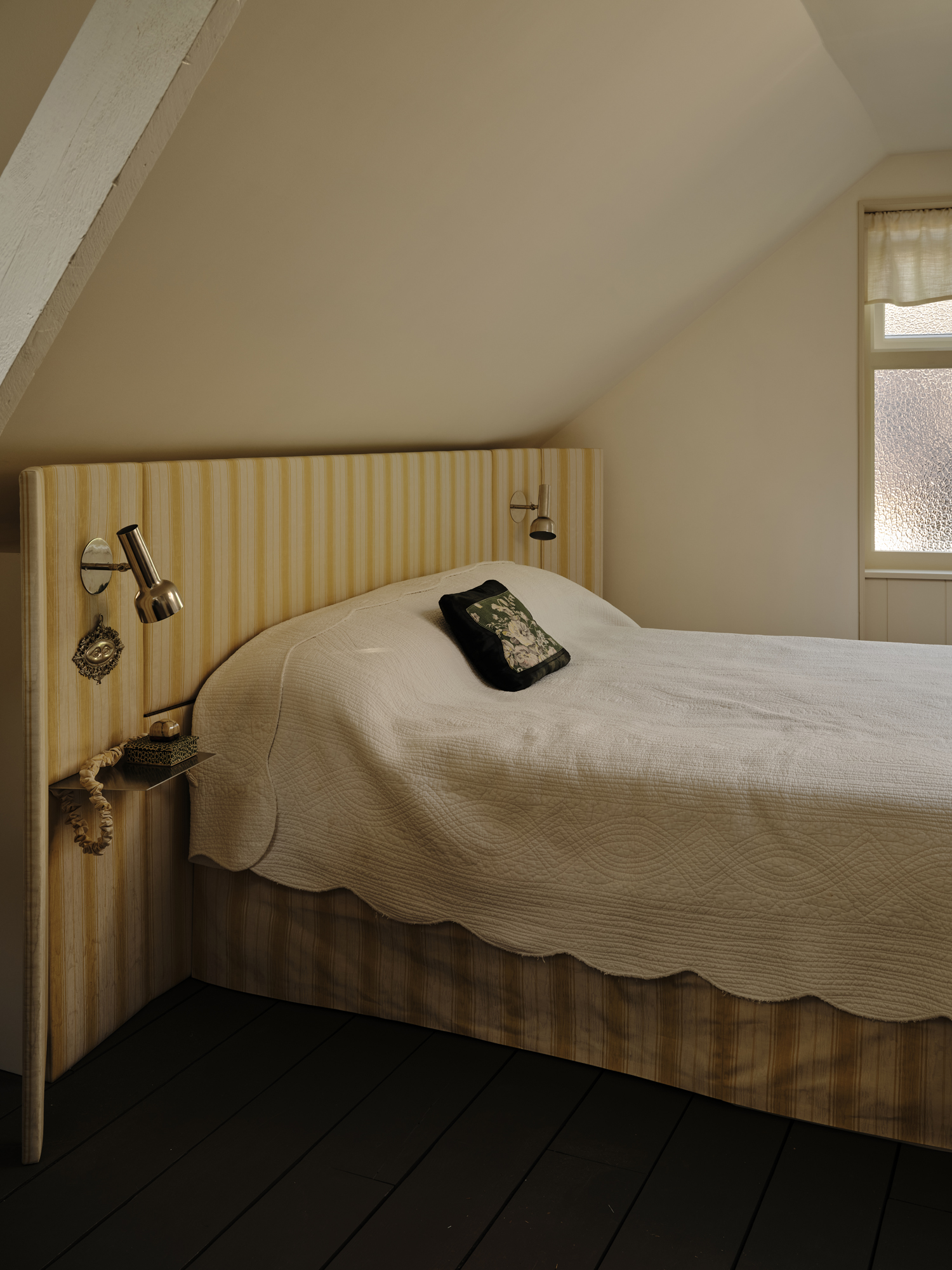 Bedroom with a light yellow striped headboard, a white quilted bedspread, and a black floral pillow.