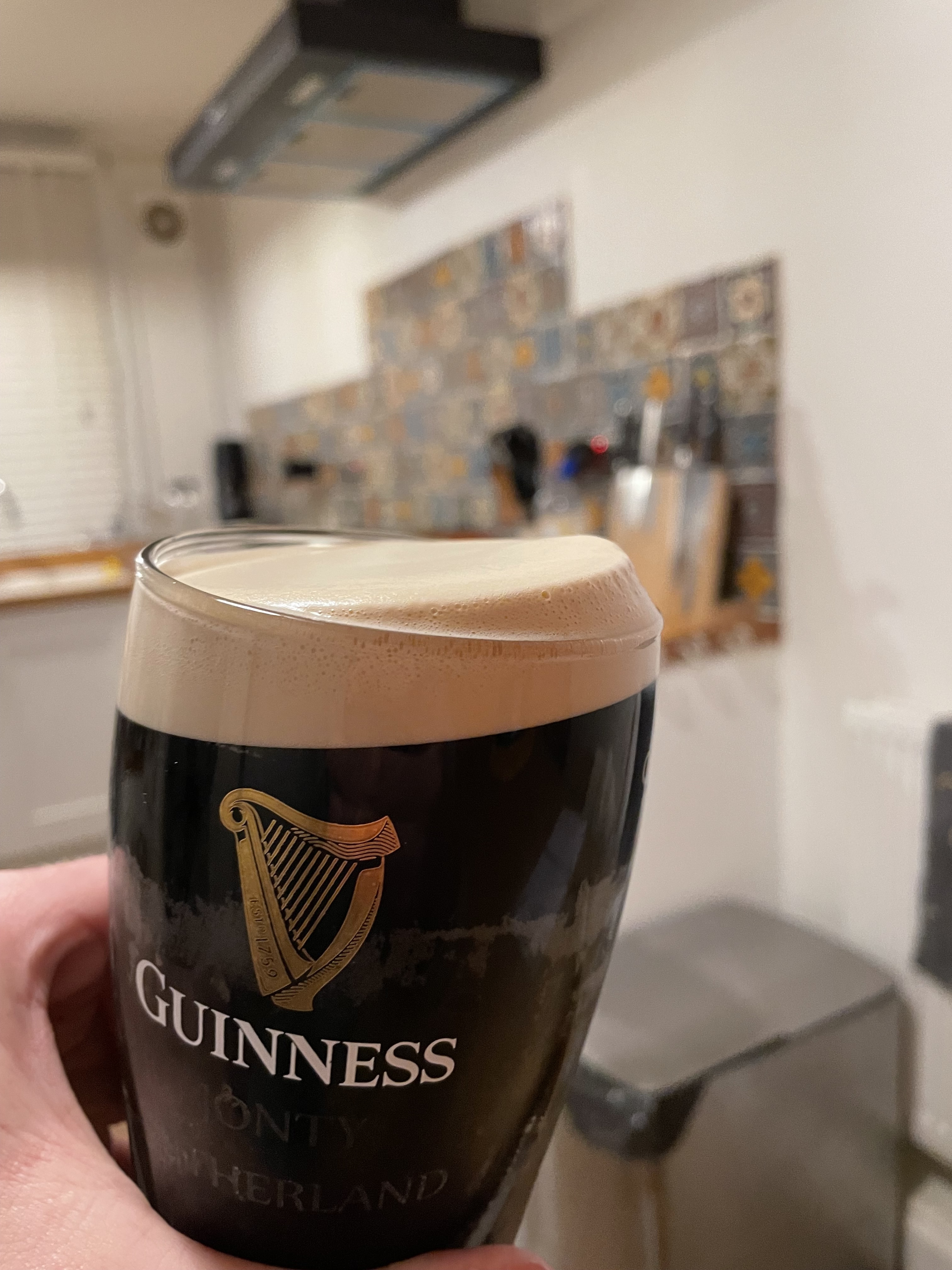 A hand holding a glass of Guinness Nitrosurge with a creamy head, poured at home.