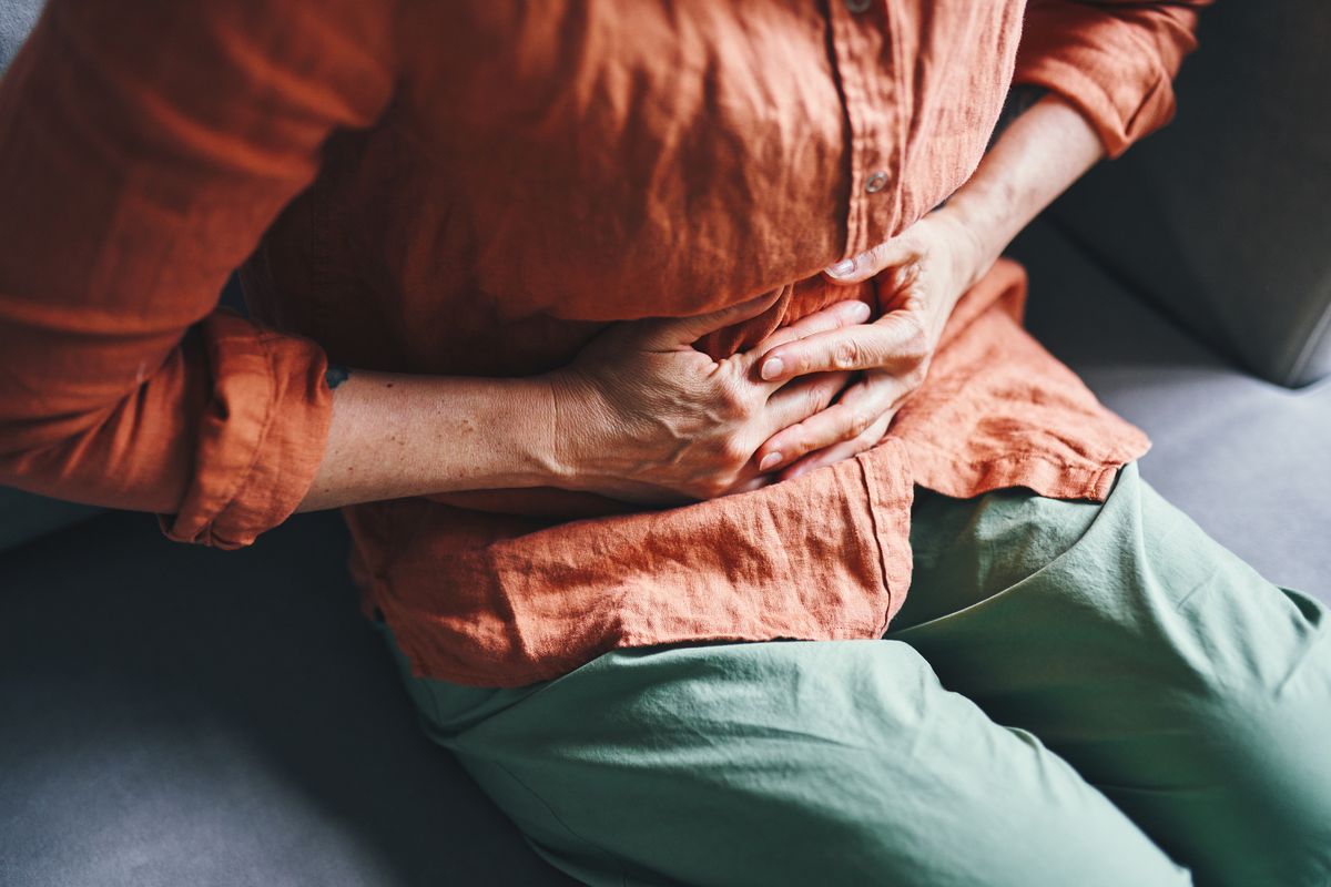 Close-up of a person holding their abdomen with a pained expression, wearing casual attire.