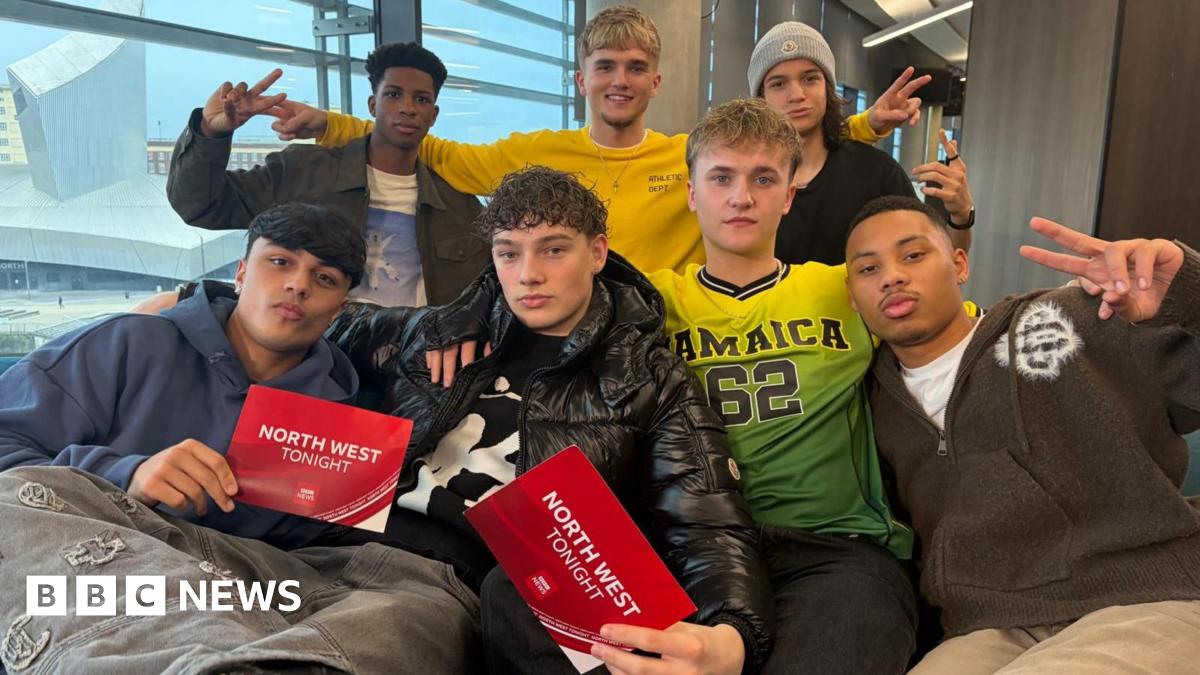 Four young men sit on a sofa with three young men standing behind them. Two of the four men who are seated are holding red cards saying 'North West Tonight'.