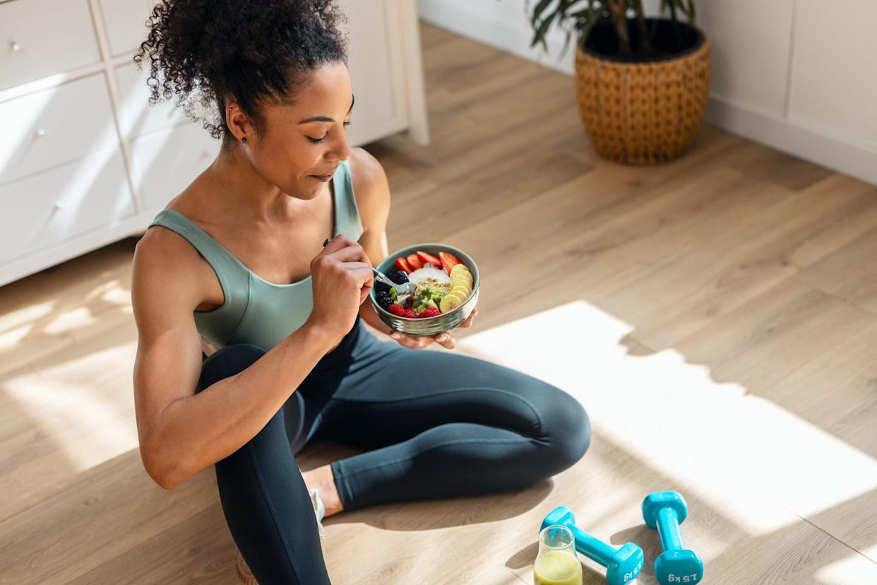 woman in workout clothes sitting on floor eating yogurt bowl