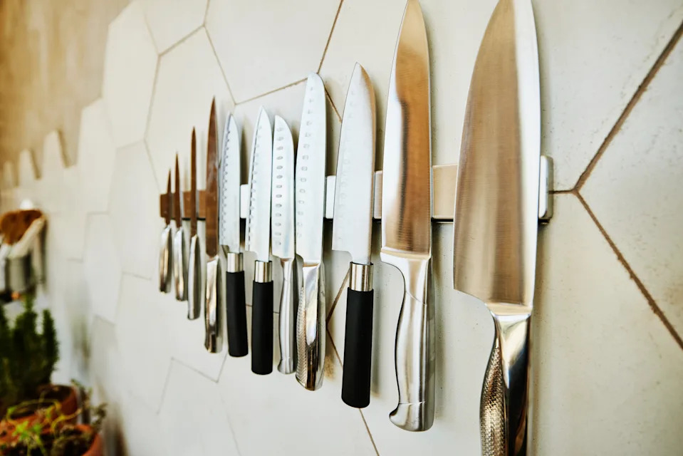 A collection of kitchen knives mounted on a magnetic strip against a tiled wall