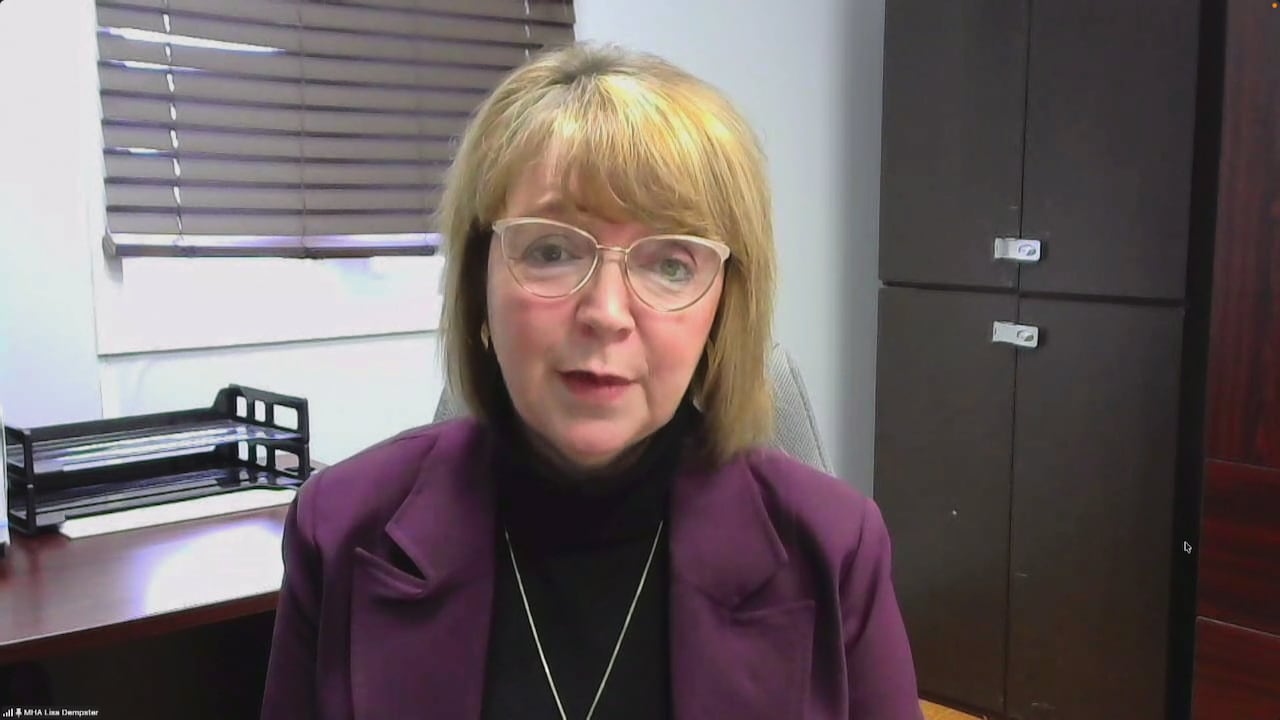 A blonde woman wearing glasses, wearing a purple suit, sits in an office in Labrador.