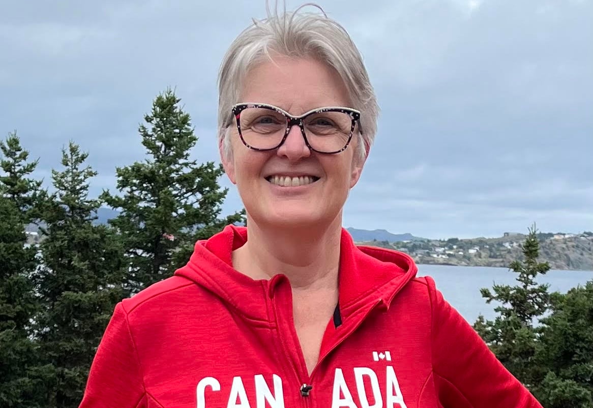 A woman wearing a red sweater stands in front of a forest.