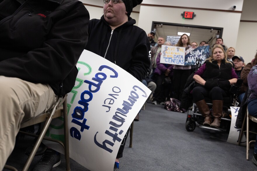 A Franklin County residents holds a sign reading “community over corporate greed” while in the background another resident holds a sign reading “save the children from data centers” during a public meeting of the zoning commission at the Franklin County Government Center in Union regarding a proposed data center near Shaw Nature Reserve.