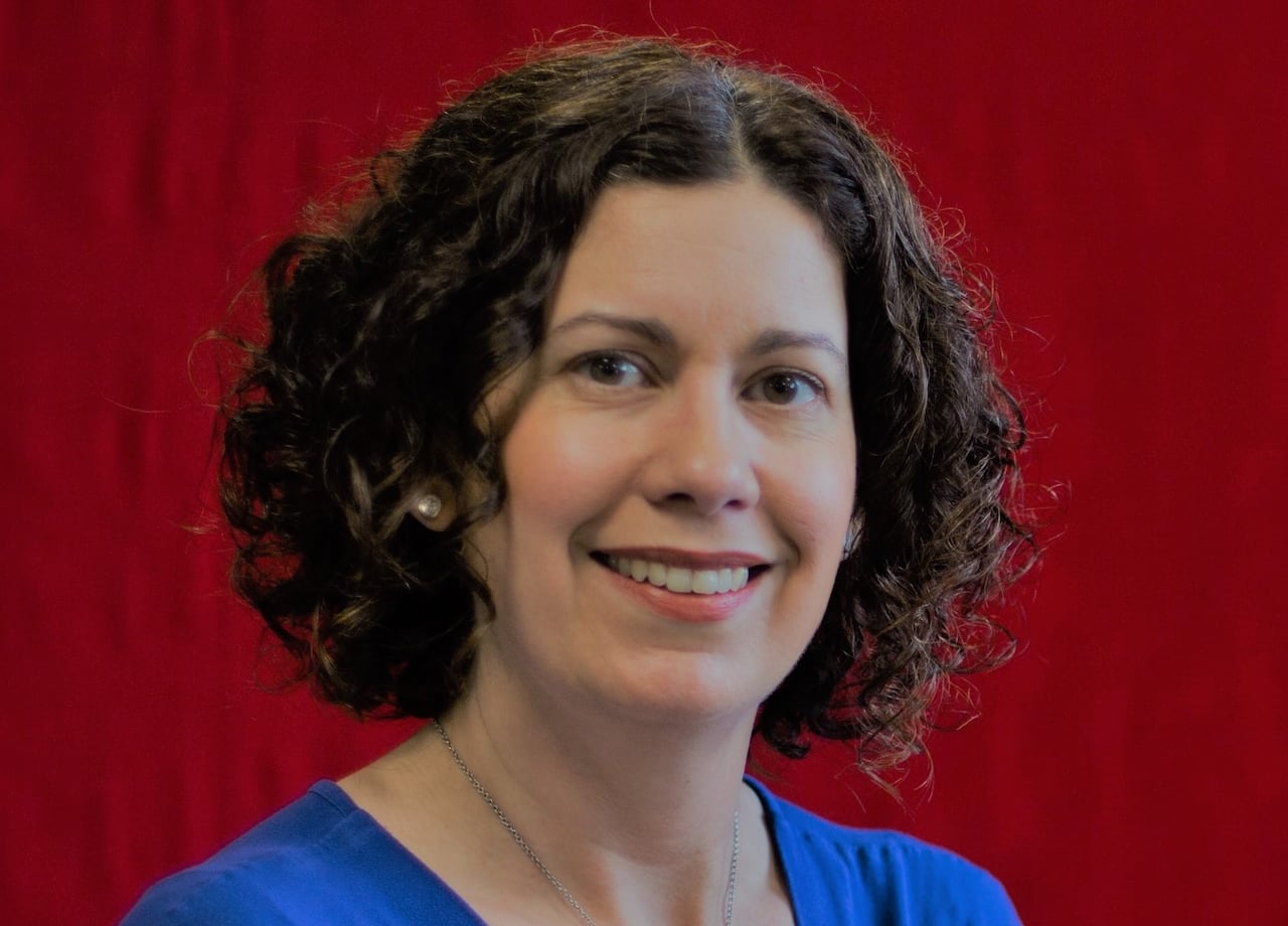 A woman with curly hair smiles in front of a red background.
